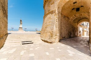 A stone pathway leading to a statue, with a clear sky and a view of the sea in the background.