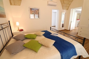 Une chambre à coucher avec un lit, des oreillers, une table de chevet, une lampe, un tableau et une vue sur un couloir.