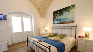 Une chambre à coucher avec un lit, une table de chevet, un téléviseur et un tableau représentant une scène de plage.
