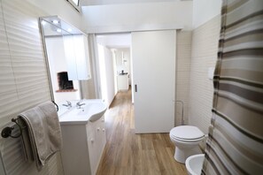 Un baño con lavamanos, espejo, toallero, inodoro y zona de ducha.