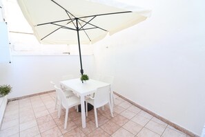 Una mesa blanca con cuatro sillas y un paraguas grande en una esquina.