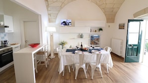 Un coin repas avec une table dressée pour six personnes, des chaises blanches, un lustre et un tableau accroché au mur.