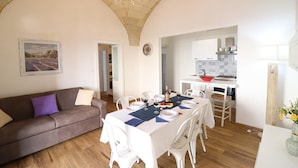 Un coin repas avec une table dressée pour deux personnes, un canapé et une cuisine en arrière-plan.