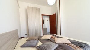 Ein Schlafzimmer mit Bett, Kissen, Nachttisch, Kleiderschrank und einer Tür.