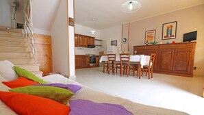 A cozy living room with a sofa, colorful cushions, a dining area with a table and chairs, a kitchen in the background, and a staircase. - Holiday Apartment "Rita" with Air Conditioning and Terrace (Otranto)