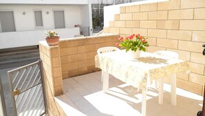 A balcony with a table and chairs, a potted plant, and a brick wall. - Holiday Apartment "Rita" with Air Conditioning and Terrace (Otranto)