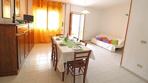 A dining area with a table set for four, a sofa with colorful cushions, and a kitchen area with wooden cabinets. - Holiday Apartment "Rita" with Air Conditioning and Terrace (Otranto)