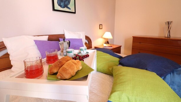 A hotel room with a bed, a bedside table with a lamp, a framed picture on the wall, and a tray with bread and a drink. - Holiday Apartment "Rita" with Air Conditioning and Terrace (Otranto)