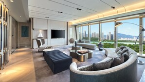 A modern living room with a large sofa, a coffee table, and a TV. There is a view of a cityscape through large windows. - Crowne Plaza Quanzhou Riverview by IHG (Quanzhou)