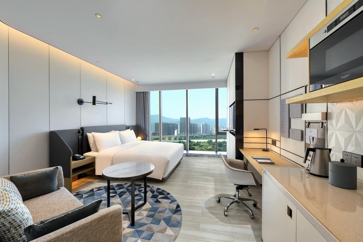 A modern hotel room with a bed, a desk, a chair, and a view of the city.