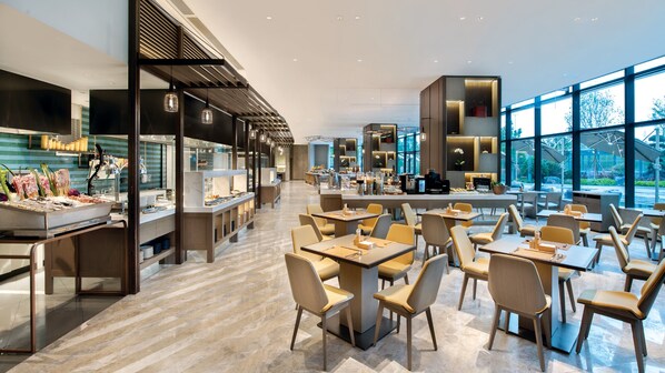 A modern restaurant with a long counter, multiple seating areas, and large windows offering a view of the outdoors.