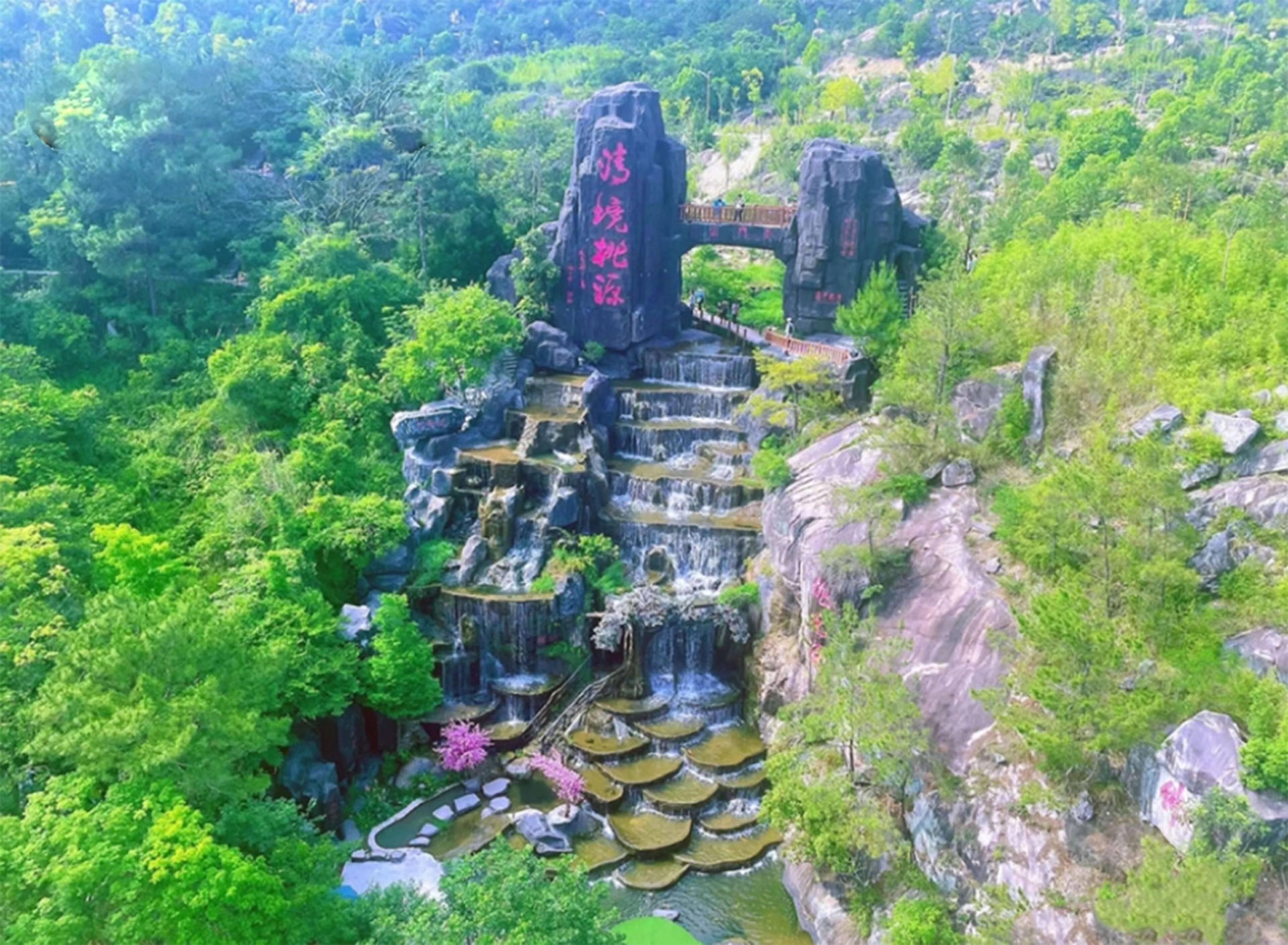 A multi-tiered waterfall structure surrounded by lush greenery and rocky terrain.