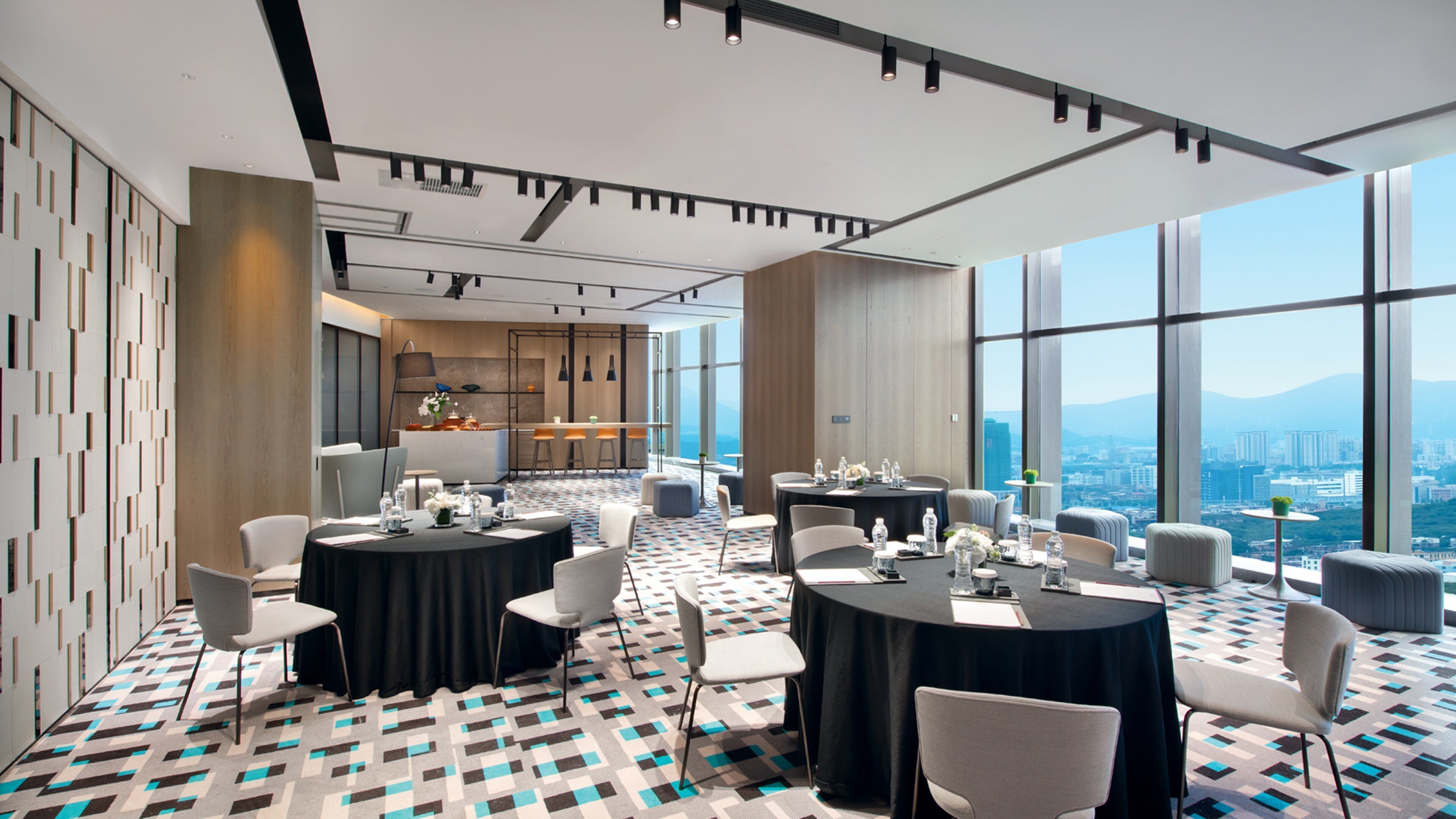 A modern conference room with round tables, chairs, and a view of a cityscape through large windows.