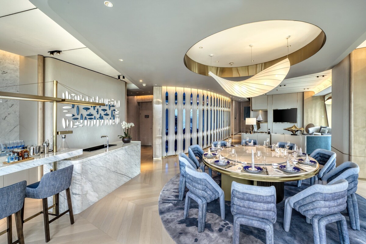 Un espace de restauration moderne avec un bar en marbre, des chaises recouvertes d’un tissu bleu et une table ronde centrale, dressée pour six personnes.