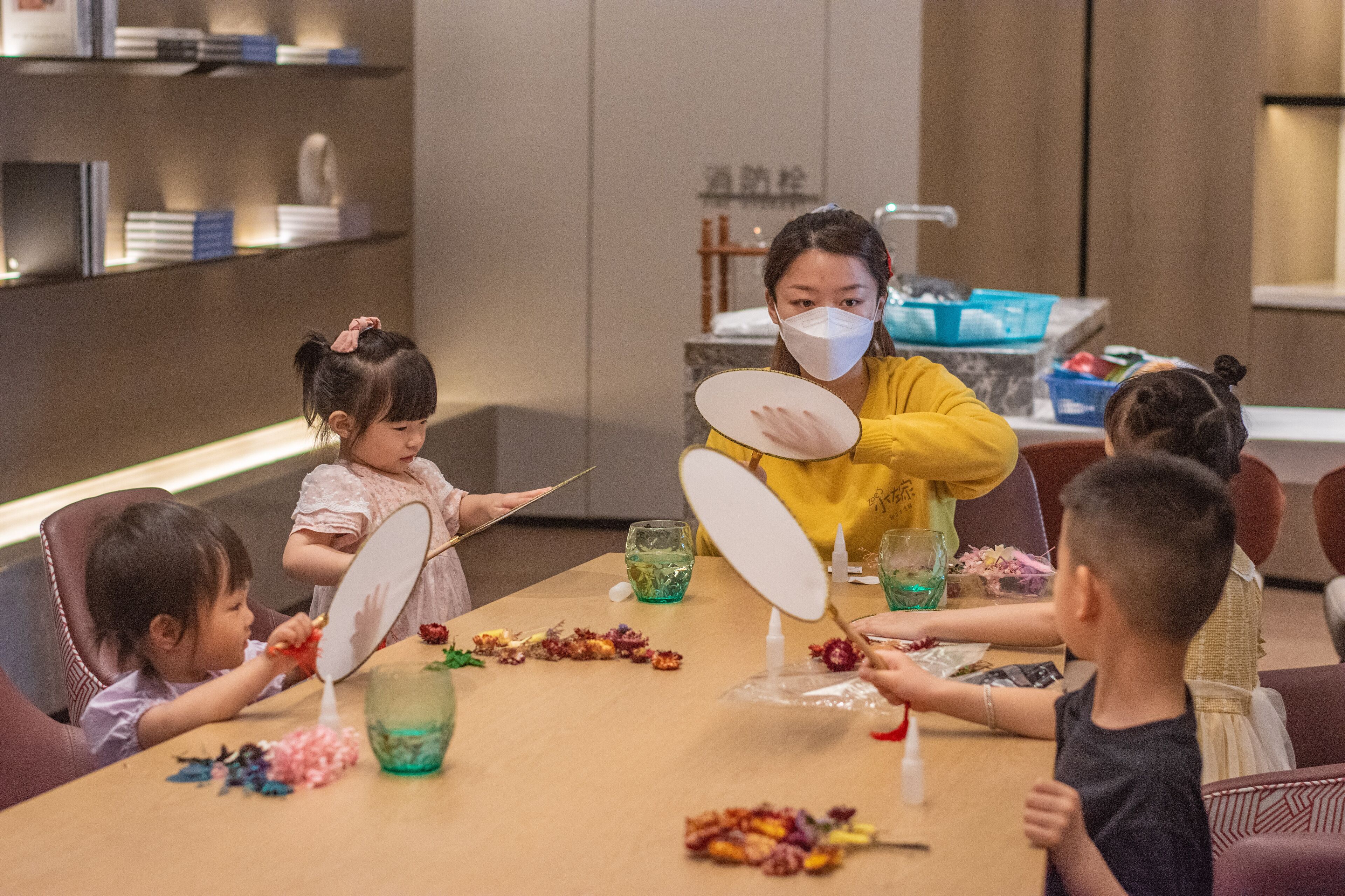 A group of children engaged in a craft activity at a table with various materials and a mirror.