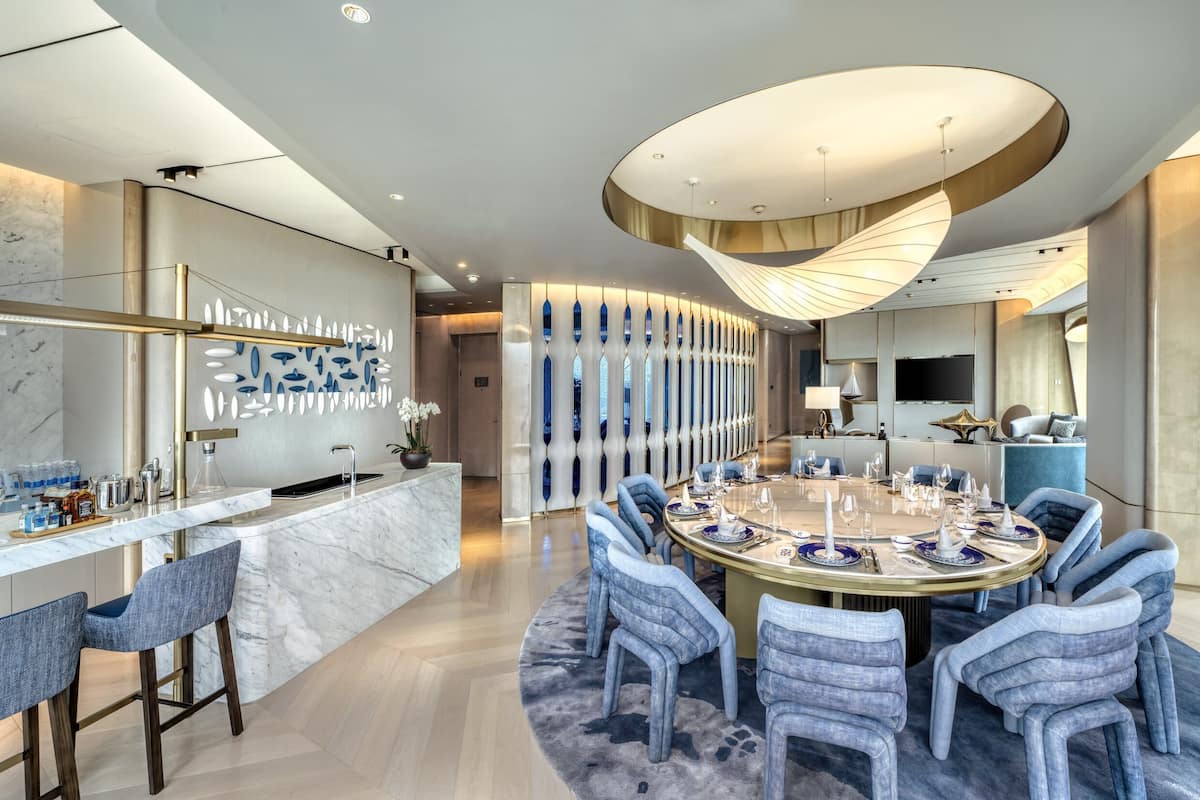 A modern dining area with a marble bar, blue upholstered chairs, and a central round table set for six.