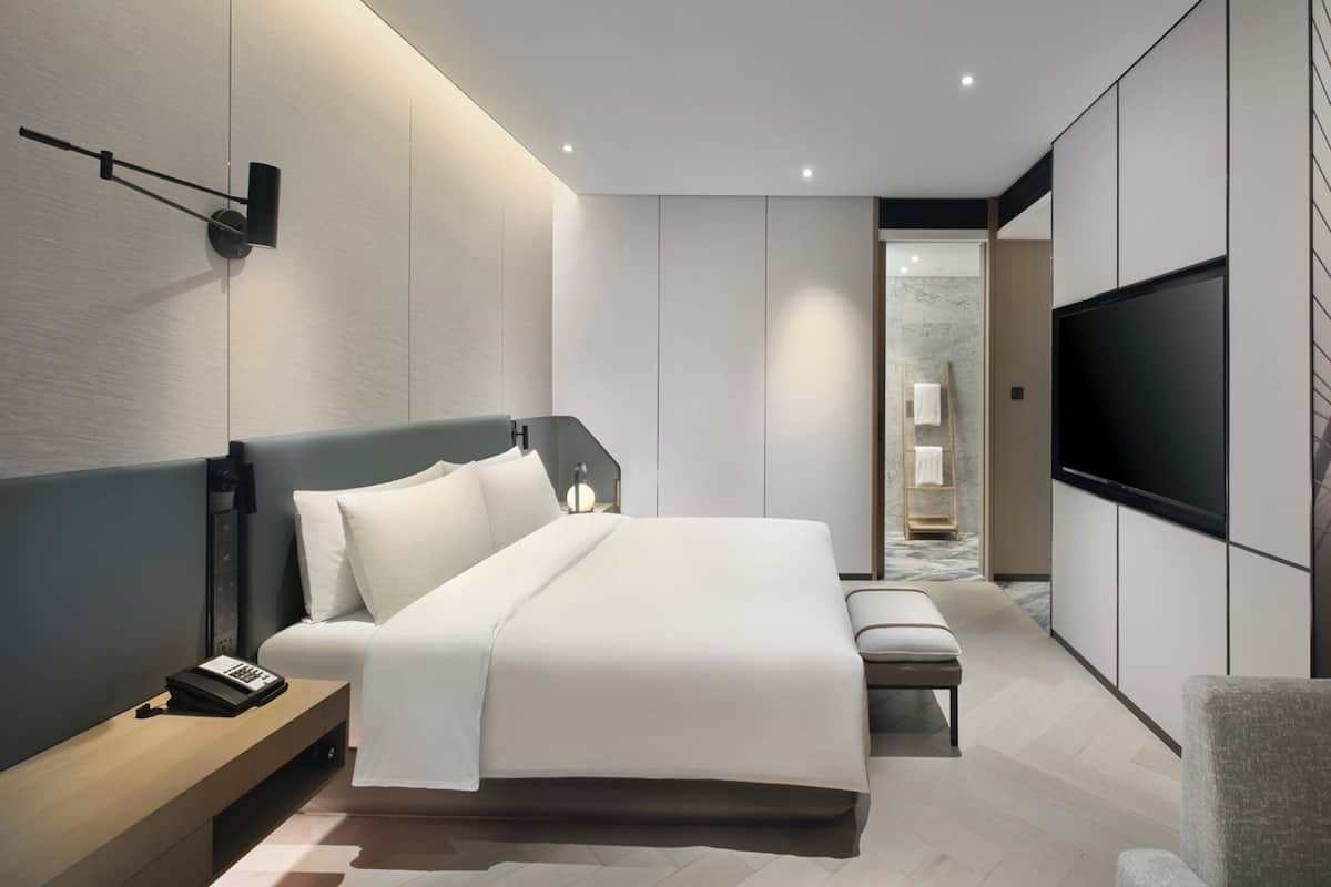 A modern bedroom with a bed, bedside table, TV, and a view of a bridge.