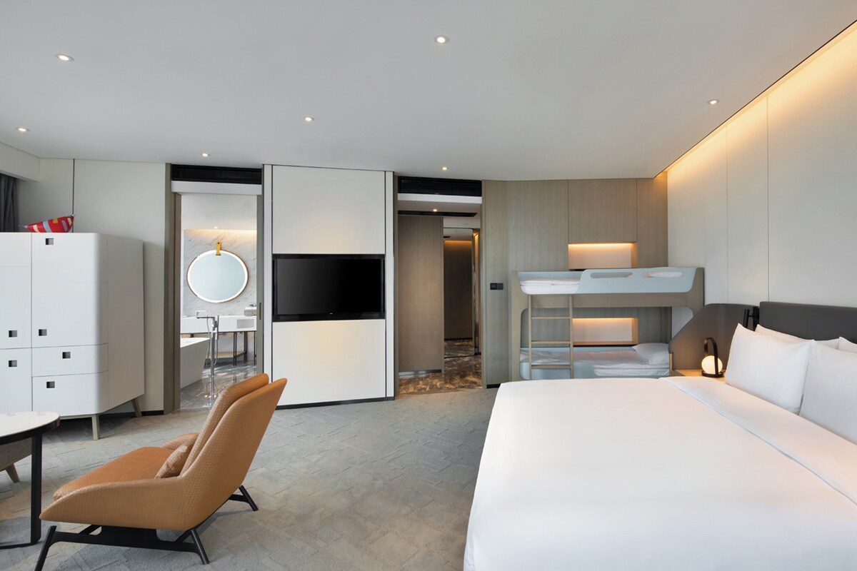 Une chambre d’hôtel moderne équipée d’un grand lit, d’une télévision, d’un bureau et d’un lit superposé.