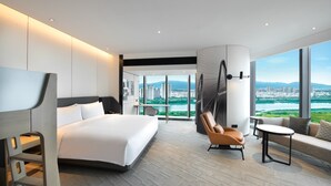 A modern hotel room with a large bed, a seating area with a view of a cityscape, and a large window. - Crowne Plaza Quanzhou Riverview by IHG (Quanzhou)