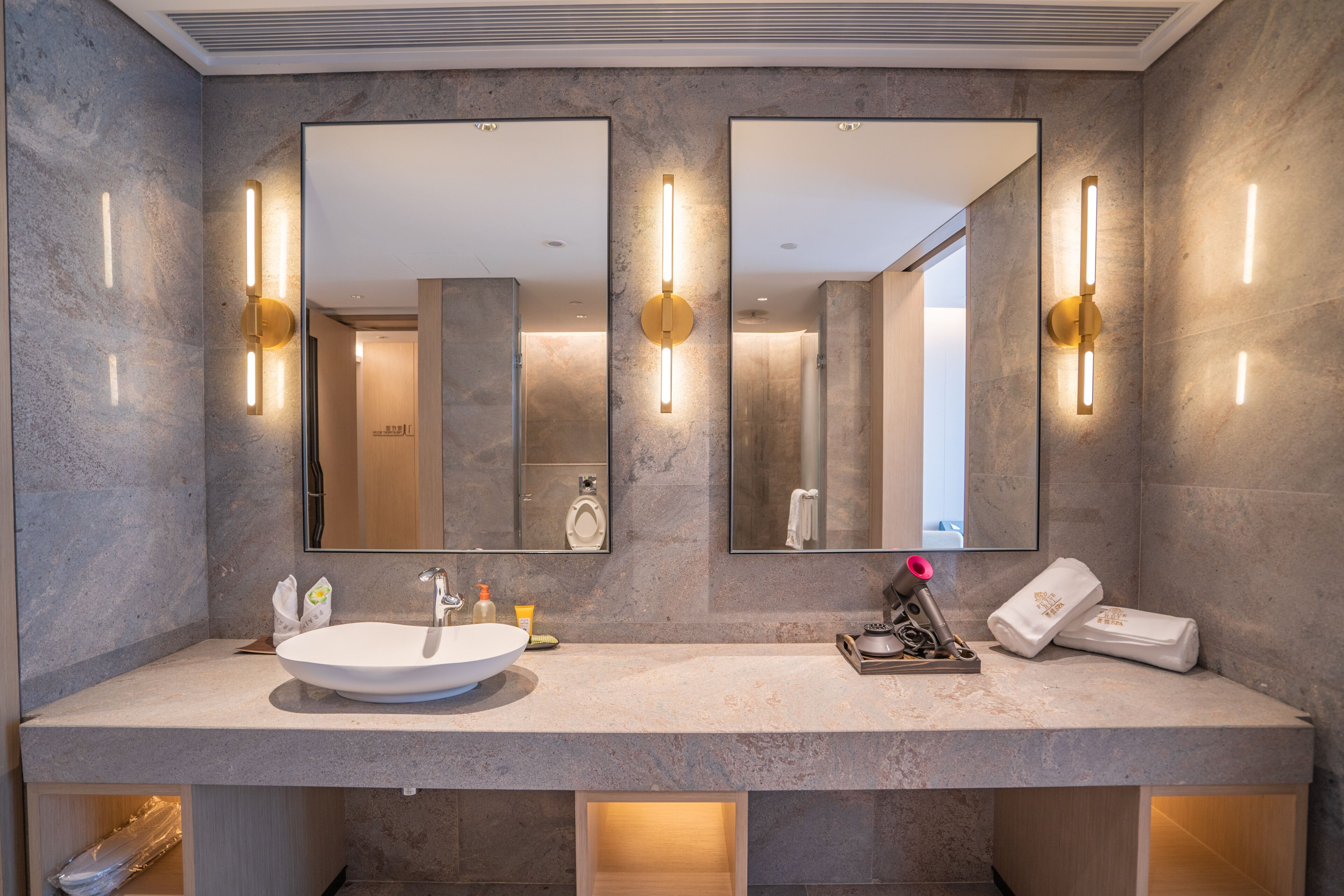 A modern bathroom with a large mirror, two wall-mounted light fixtures, a sink, and a towel rack.