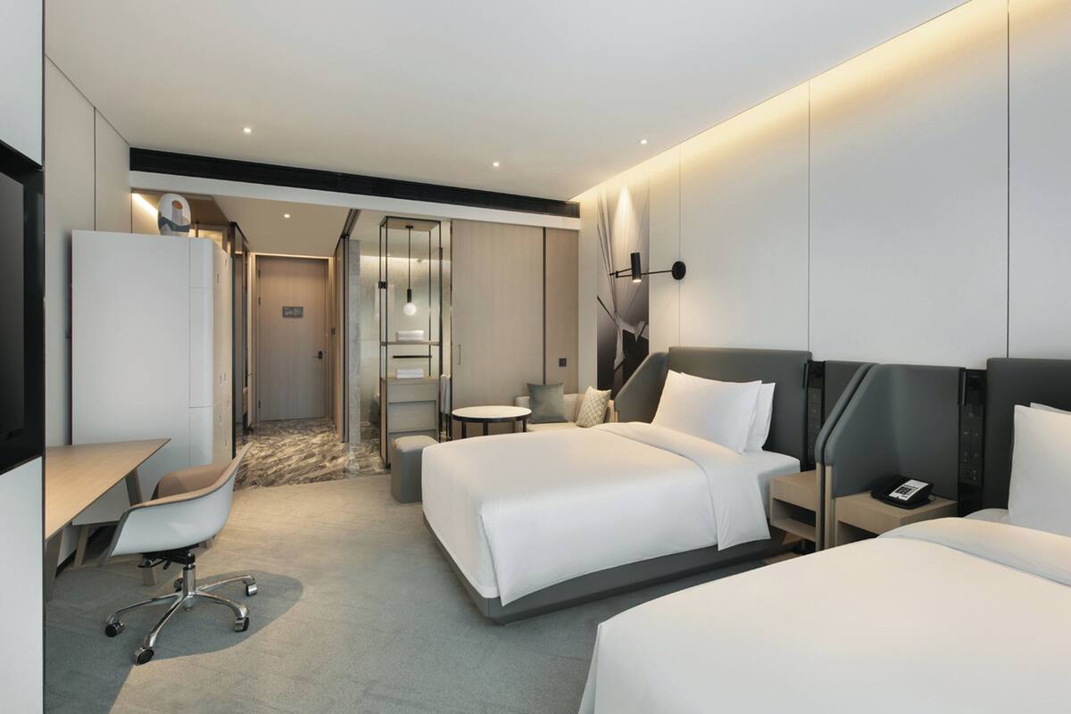 A modern hotel room with two beds, a desk, and a small seating area.