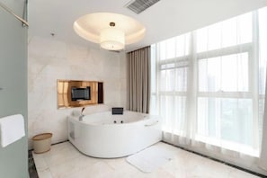 A modern bathroom with a freestanding bathtub, a large mirror, and a television mounted on the wall.