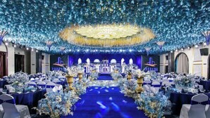 A banquet hall with a central stage, rows of tables with blue tablecloths and white chairs, and a ceiling adorned with blue foliage and lights. - Tianfu Howard Easy Hotel (Funan)