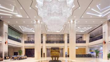 A spacious lobby with a high ceiling, a central reception desk, and a large chandelier.