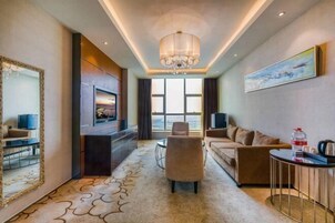 A modern hotel room with a large window, a chandelier, a sofa, a TV, and a coffee table.