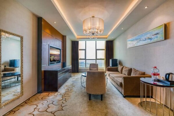 A modern hotel room with a large window, a chandelier, a sofa, a TV, and a coffee table.