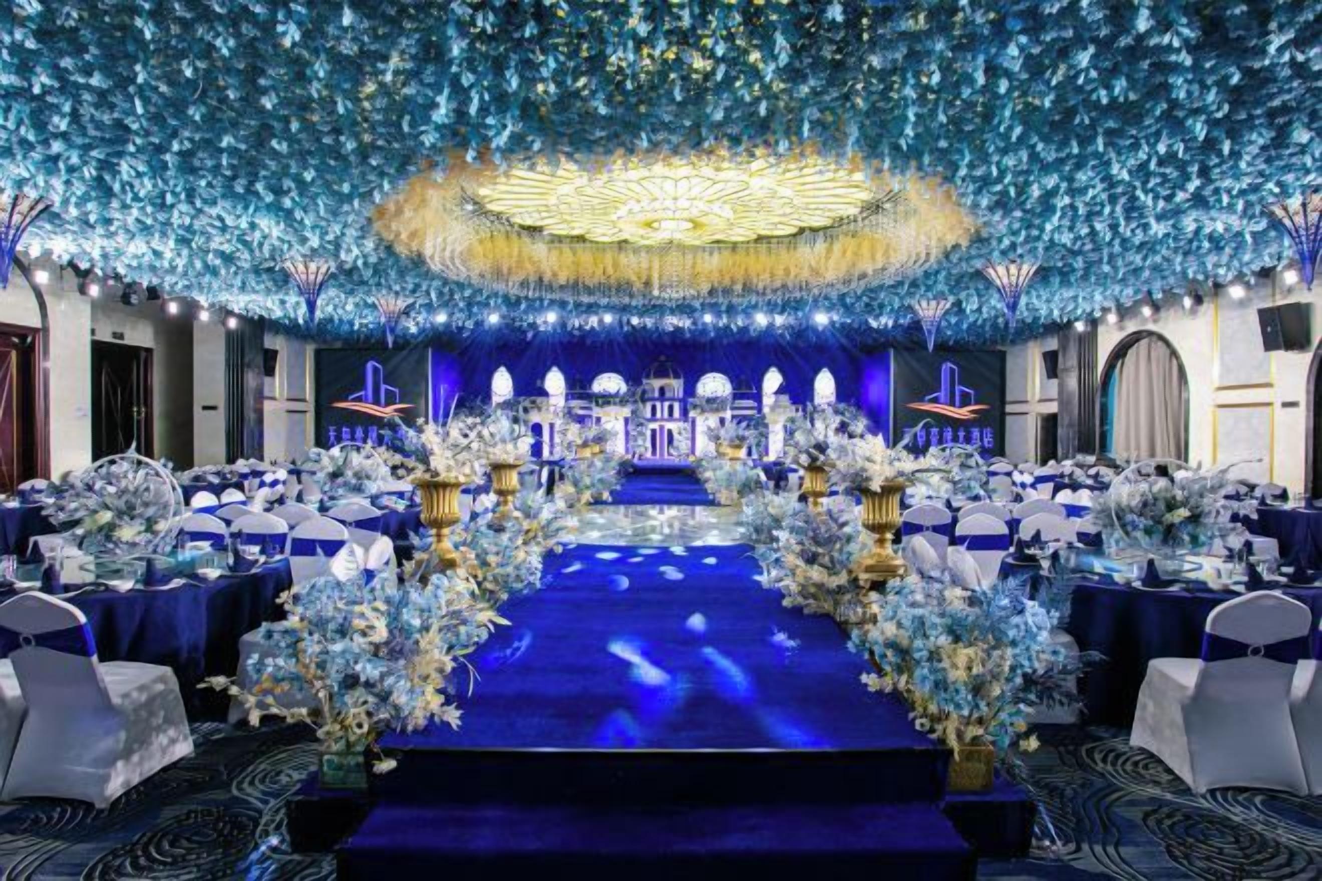 A banquet hall with a stage, tables, and floral decorations.