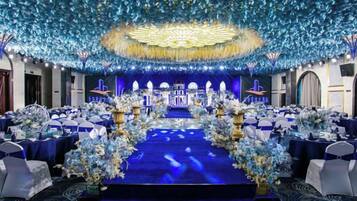 A banquet hall with a stage, tables, and floral decorations.