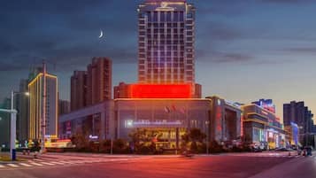 A modern hotel with a prominent tower, a large glass facade, and a well-lit street in the foreground.