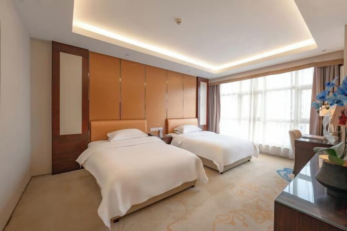 A hotel room with two beds, a large window, and a modern ceiling design.