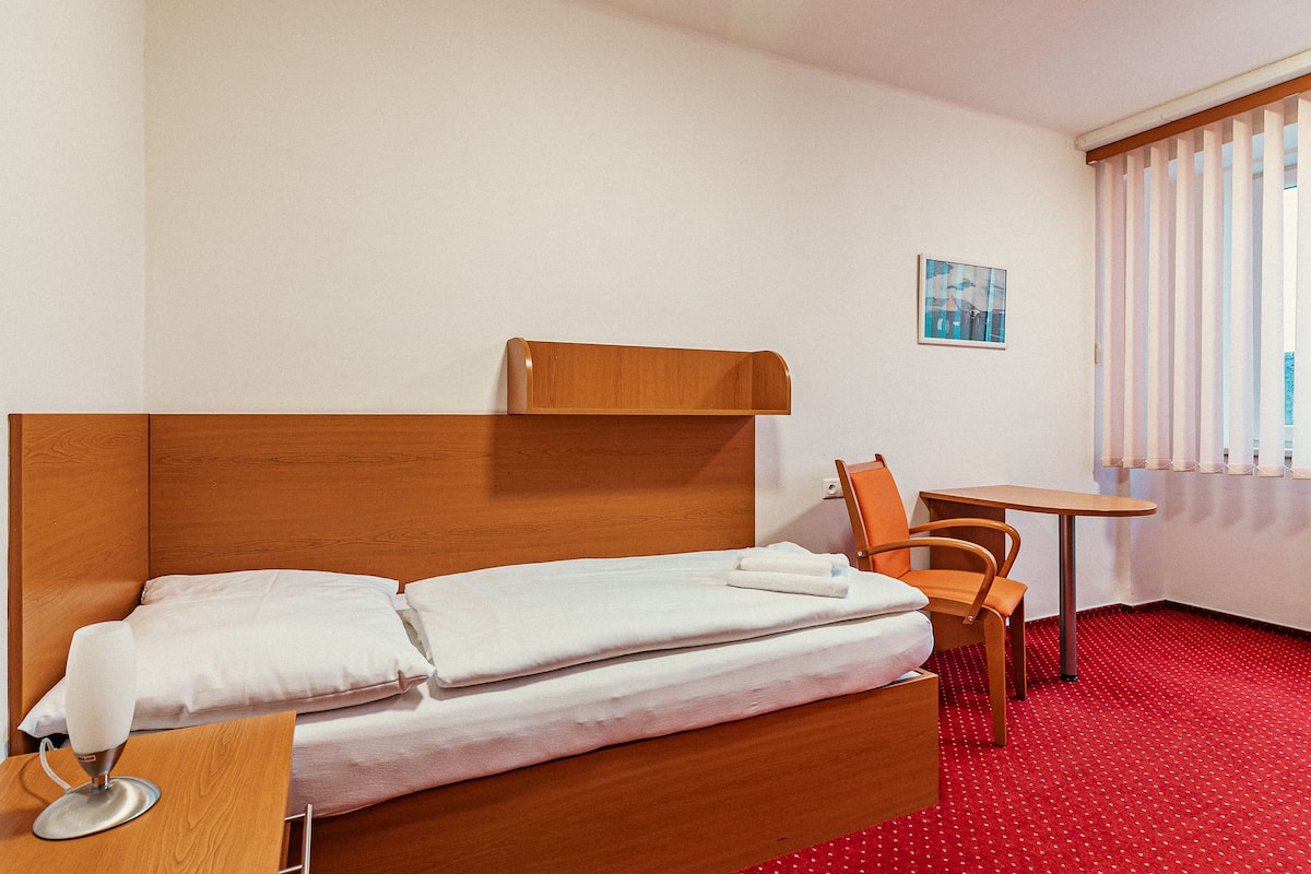 A hotel room with a wooden bed, white linens, a small table, and a chair.