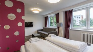 Habitación de hotel con dos camas, un sofá, un televisor y una ventana con cortinas.