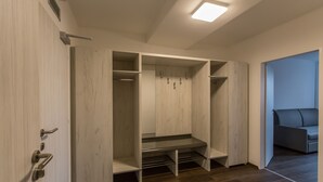 Un vestidor con repisas abiertas y un banco, una puerta con picaporte, y una pared azul de fondo.