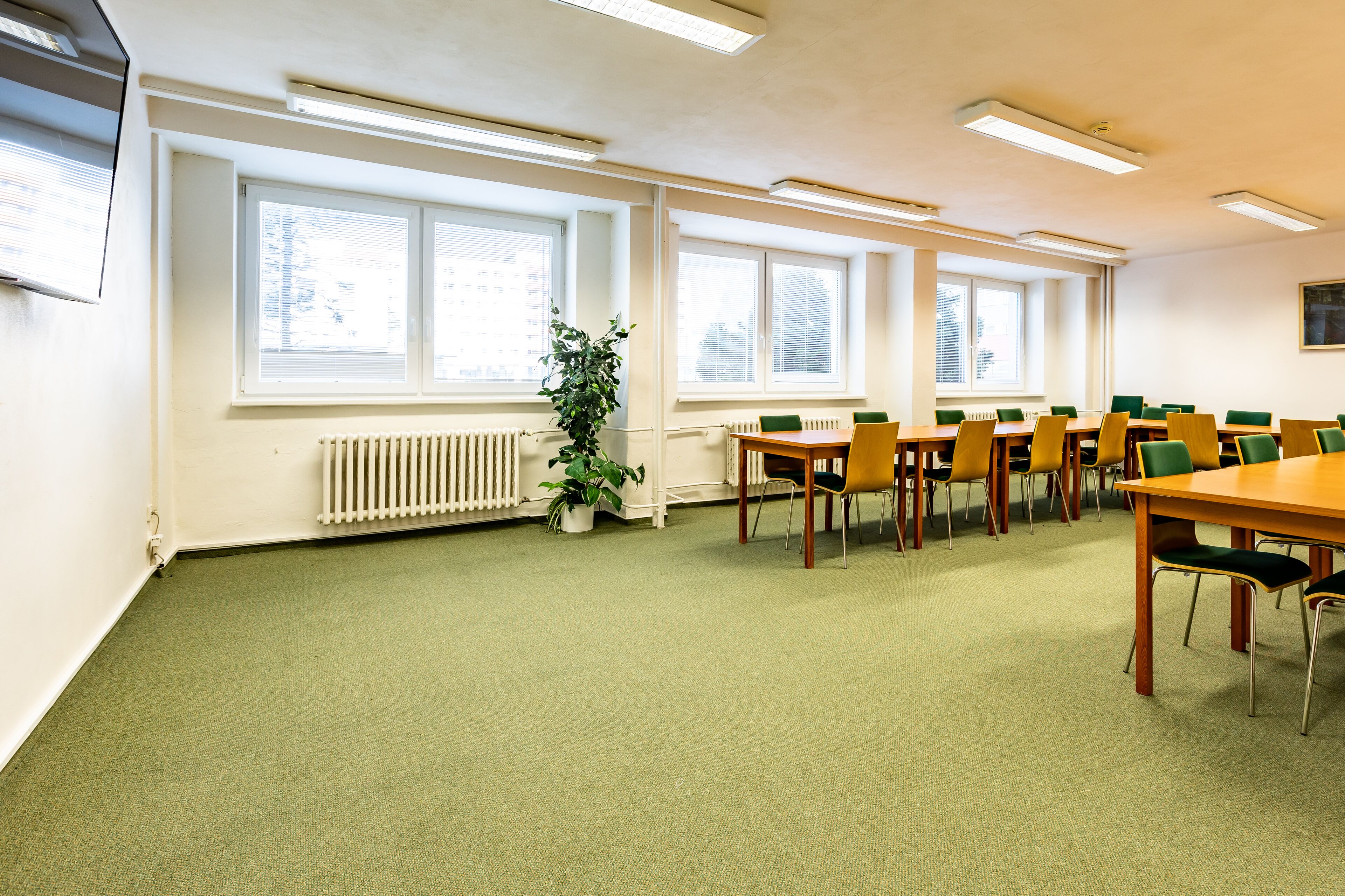 A conference room with a long table, multiple chairs, large windows, and a radiator.
