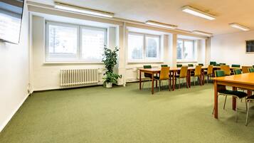A conference room with a long table, multiple chairs, large windows, and a radiator.