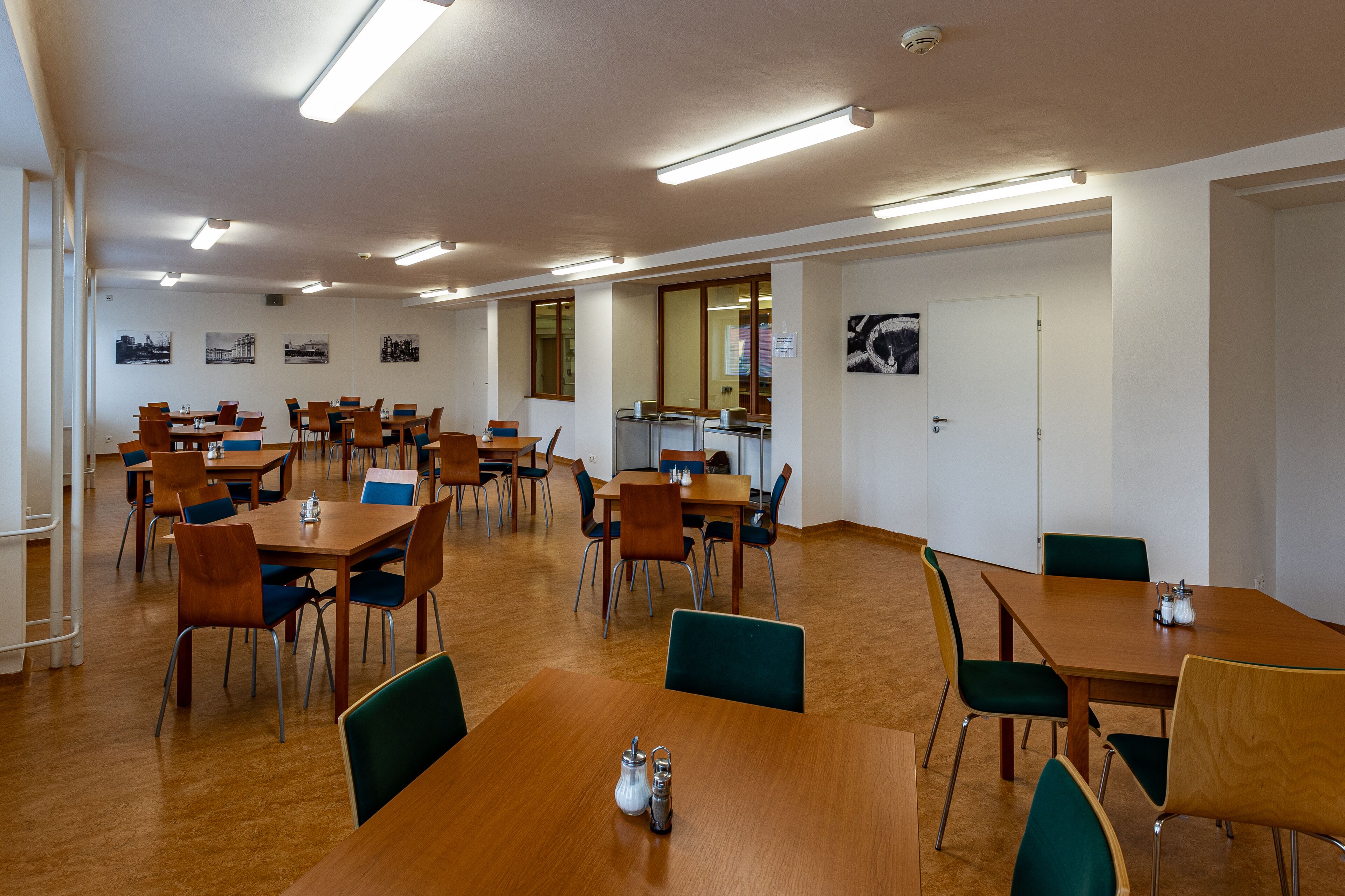 A spacious dining area with multiple tables and chairs, a wooden floor, and ceiling lights.
