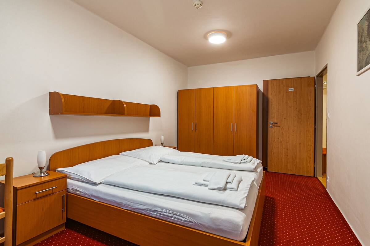 A hotel room with a wooden bed, a wooden wardrobe, a wooden nightstand, and a red carpeted floor.