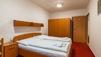 A hotel room with a wooden bed, a wooden wardrobe, a wooden nightstand, and a red carpeted floor.
