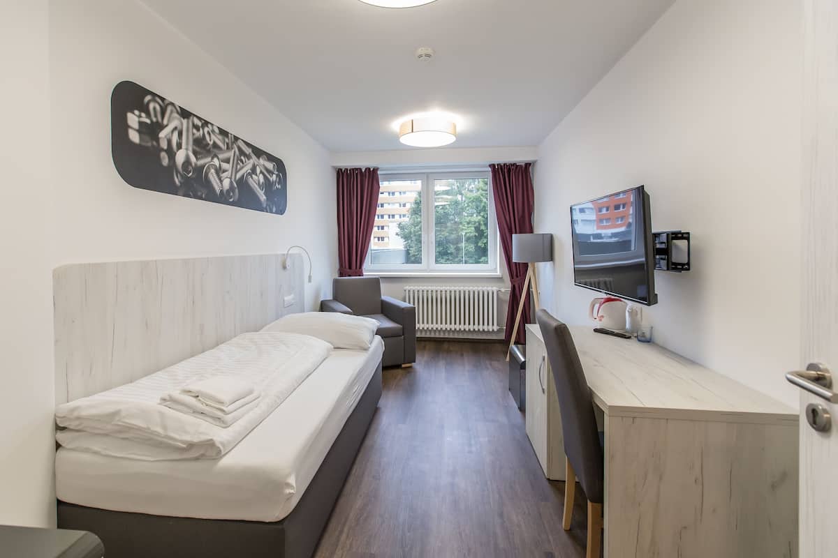A hotel room with a bed, a desk, a chair, a television, and a window with curtains.