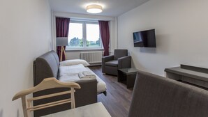 Una habitación de hotel moderna con una cama sofá, una mesita, una silla y un televisor montado en la pared.