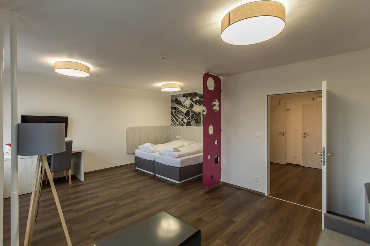 A modern bedroom with a bed, a desk, and a chair. There is a door leading to another room.