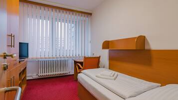 Habitación de hotel con cama, escritorio, silla, televisión y ventana con persianas.