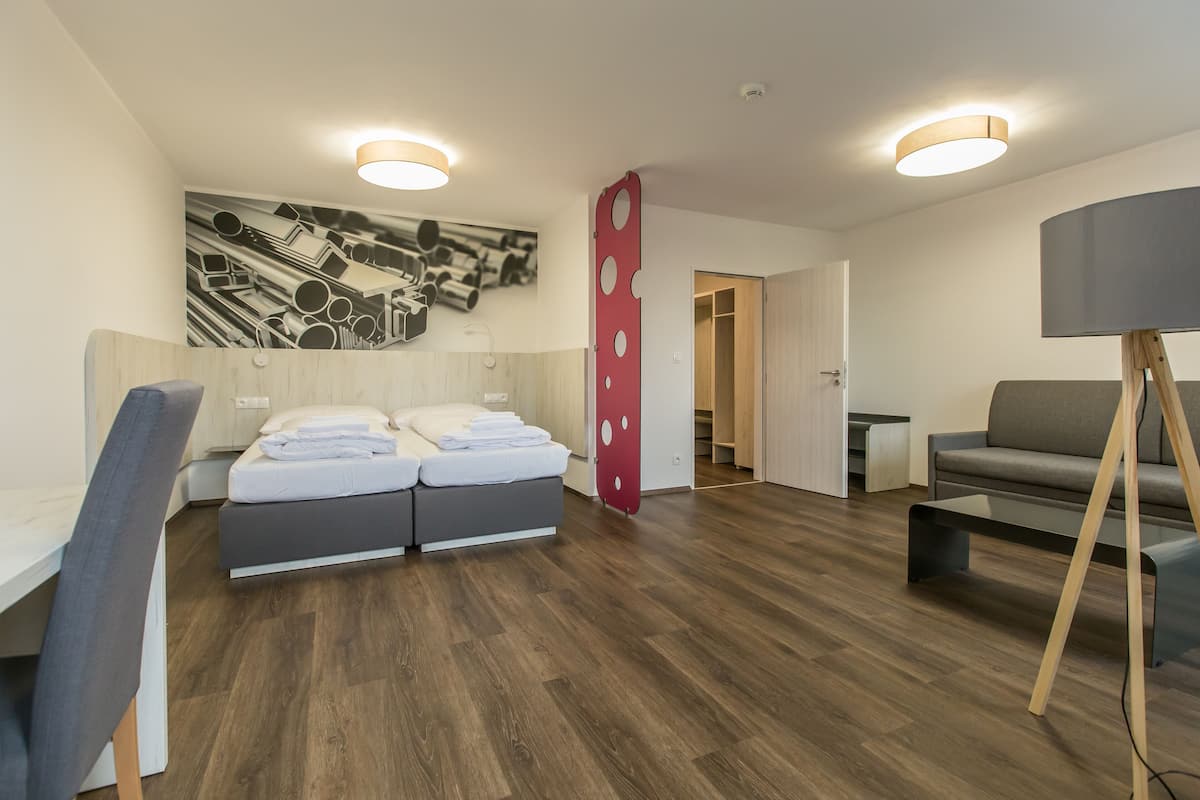 A modern hotel room with a double bed, a desk, a chair, a sofa, and a TV on a stand.