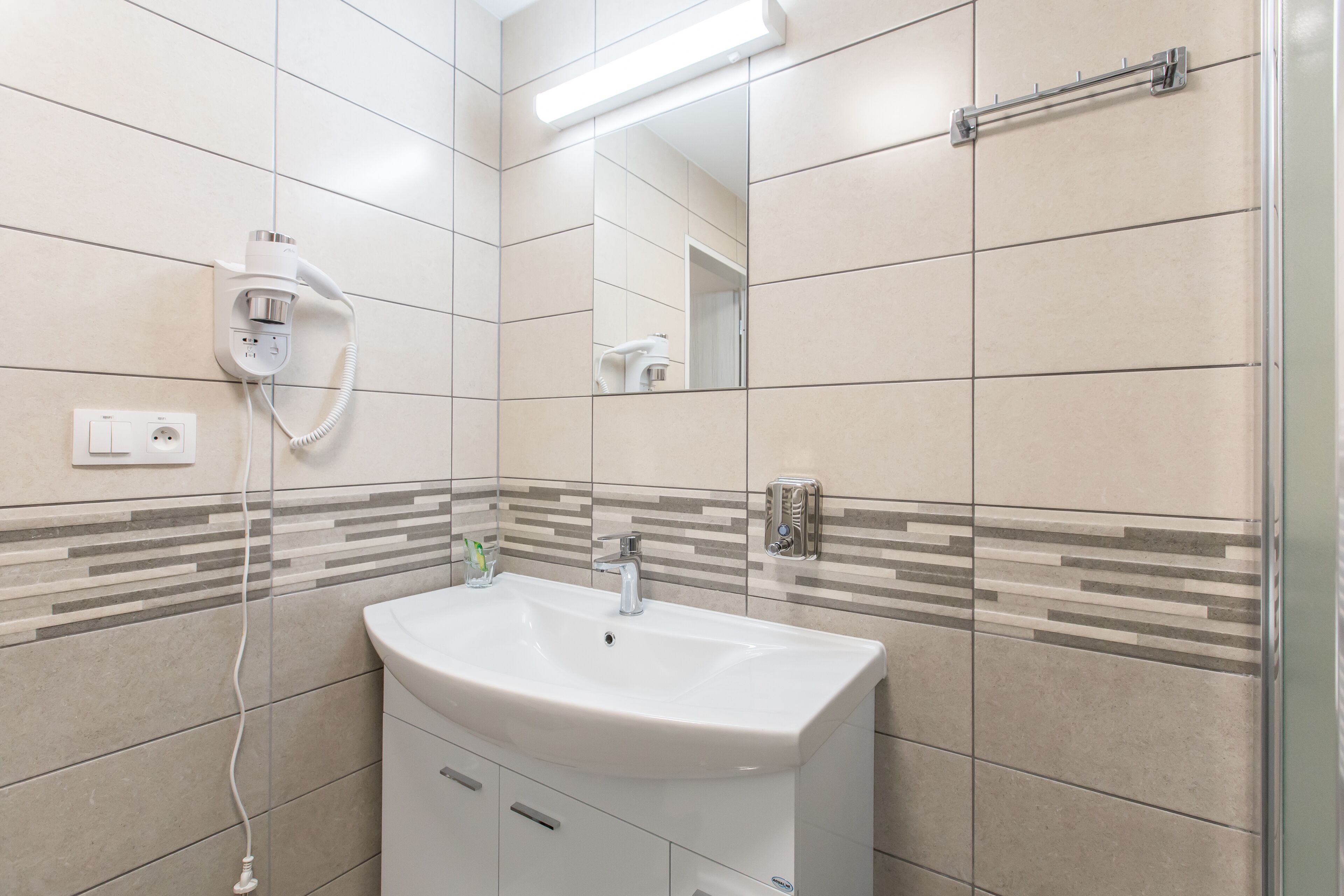 Un baño moderno con un lavamanos blanco, un espejo y un secador de pelo fijado en la pared.