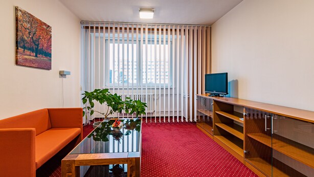 A modern living room with a red carpet, orange sofa, glass coffee table, and a TV on a wooden stand. - Hotel Garni VŠB (Ostrava)