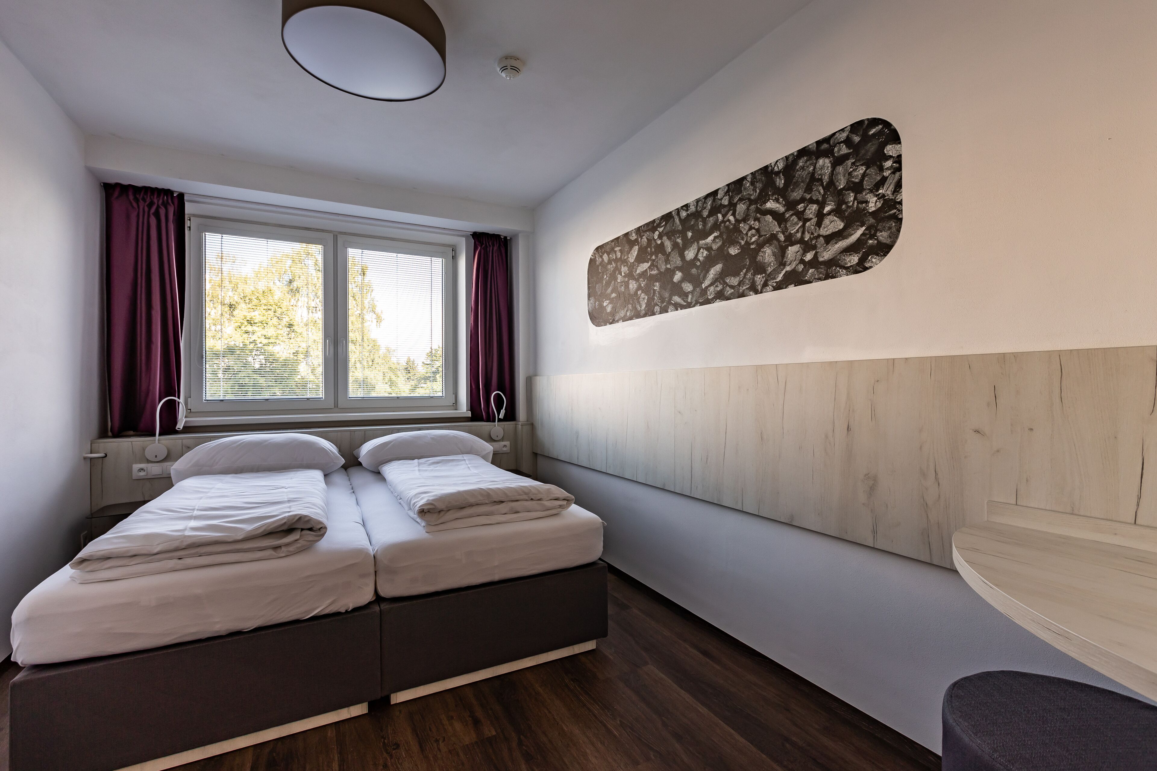 Une chambre à coucher moderne avec un lit, une fenêtre avec des rideaux, une œuvre d’art accrochée au mur et un banc intégré.